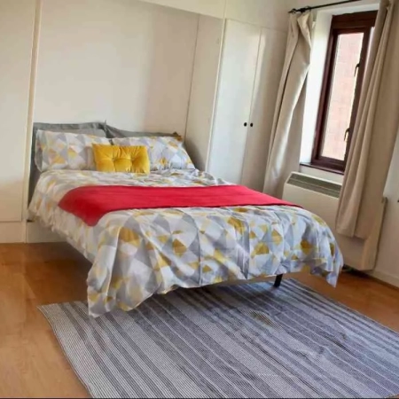 A double bedroom with pillows, bedding, a carpet , built-in wardrobes, mirror and large window.