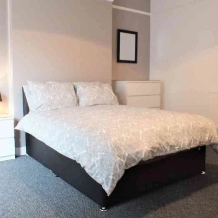 An ensuite room with a double bed, bedding, pillows, 2 bedside tables, and 2 wall frames.