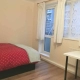 A double bedroom with red bedding, large windows, white curtains, a table and a chair.
