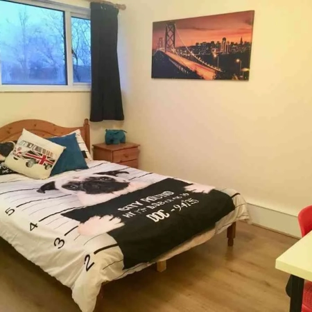 A double bedroom furnished with bedding, pillows, two bedside tables, a window, curtains, a table, a chair and a wall frame.