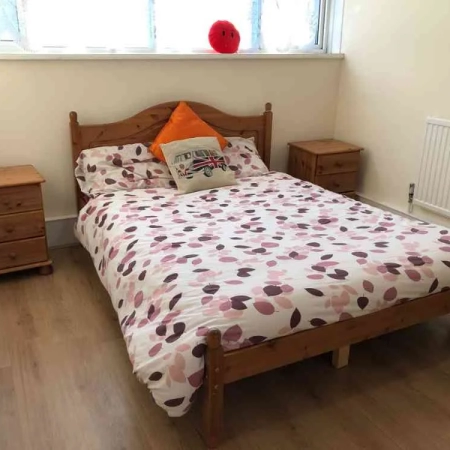 A double bed with bedding, pillows, 2 bedside tables, and a window positioned at the top of the bed.