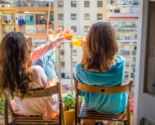 In this Flatsharing Success Tips blog, two women are seated, facing outward, each holding a drink, sharing a cheerful toast.