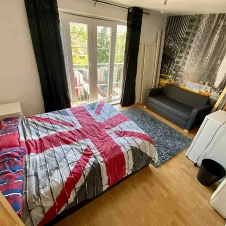 A fully furnished room in Peckham with a double bed, fridge, sofa and a glass door leading to a balcony.