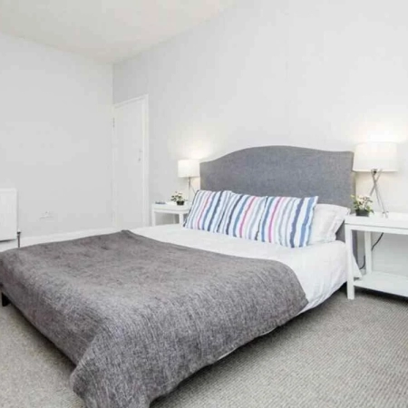 The bed in this room near Brixton Station is adorned with grey bedding and pillows, flanked by two bedside tables featuring lamps.