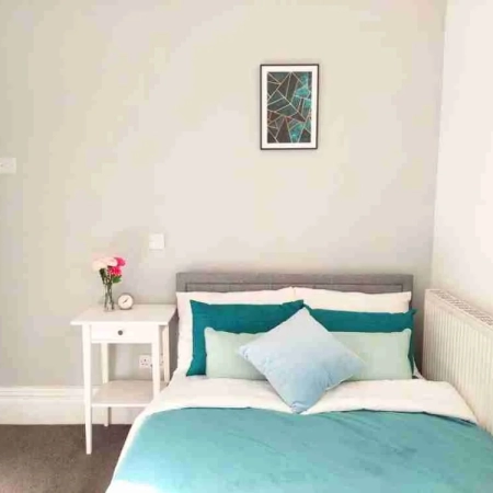 In this double room in Balham London, the bed was adorned with green bedsheets, and pillows were neatly arranged on top and a bedside table.
