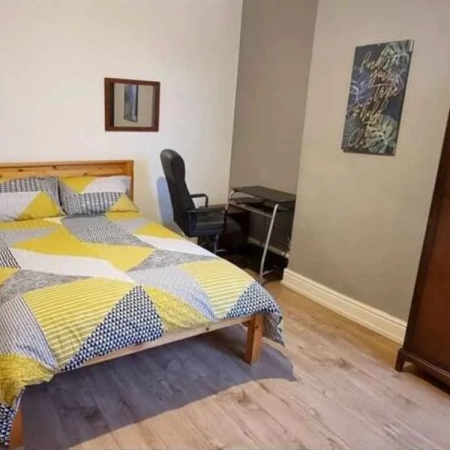This double bedroom in Central London includes a bed with bedding, a chair and a side table, all adjacent to the wardrobe.