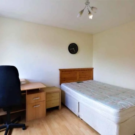 This double room near Stockwell Station is equipped with a bed, bedside table, table, office chair, and wall clock.