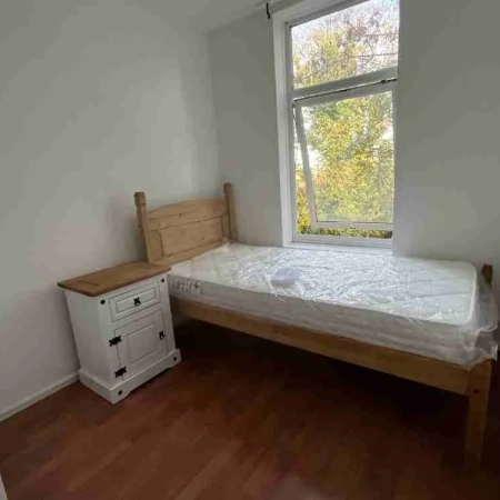 This furnished single room for rent includes a bed with a window on the right and a bedside table on the left.