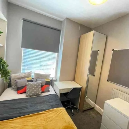 The Zone 2 double room features a bed with pillows and a window above. On the right side, there is a table, chair, and wardrobe. A cabinet is positioned in front of the wardrobe.