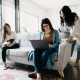 Two women are sitting while one is standing in a living area in the blog on flatshare living with strangers.