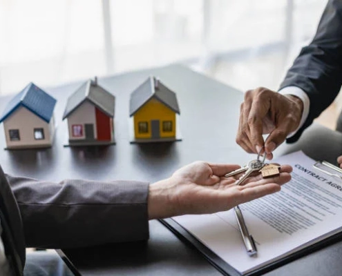 A hand passing a key to another hand against the backdrop of three display houses in the 'Landlord's Success with Rent-Guaranteed' blog