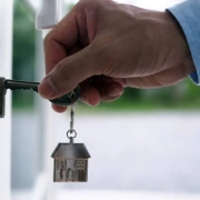 A hand, holding a key with a house keychain, is inserting it into a door in the 'London's Guaranteed Rent Growth' blog.