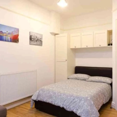 This double bedroom near Clapham Station features a bed adorned with bedding and a pillow. It is enclosed by cabinets, with a door situated on the right side.