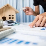 A man with paperwork with a house model on a background on the guaranteed rent for Landlords blog.