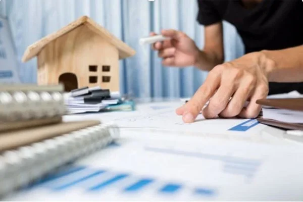 A man with paperwork with a house model on a background on the guaranteed rent for Landlords blog.